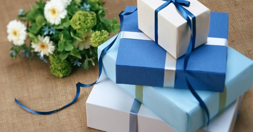 Three beautifully wrapped gift boxes with blue ribbons arranged beside a floral bouquet.